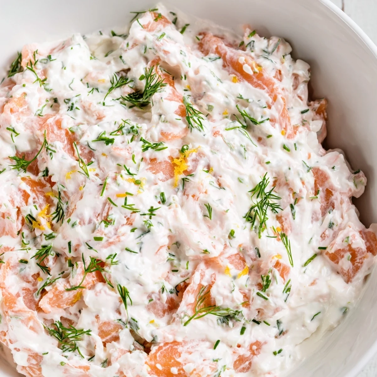 A creamy bowl of Smoked Salmon Dip garnished with fresh dill, lemon zest, and served with crisp cucumber slices and crackers for dipping.  