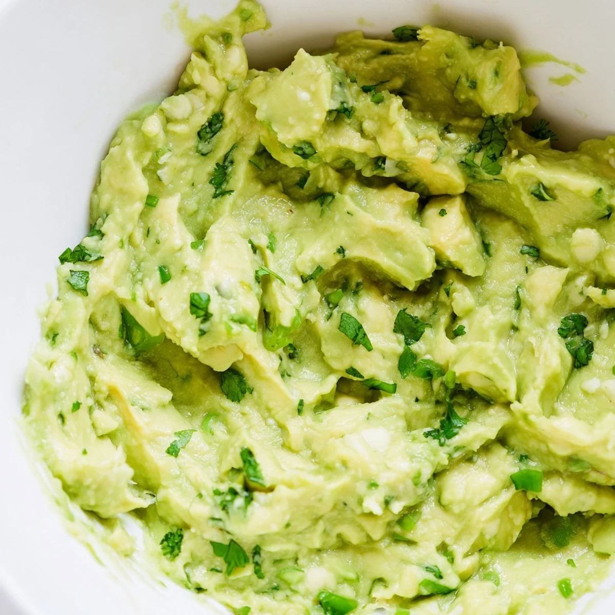 Creamy avocado lime dip in a rustic bowl surrounded by tortilla chips and sliced jalapeños.