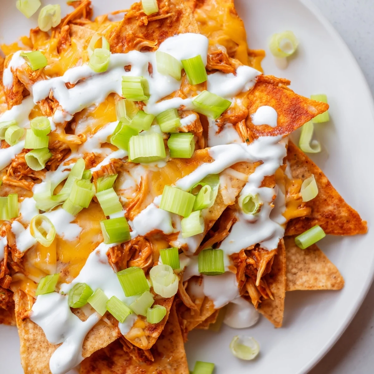 Tortilla chips piled with spicy Buffalo chicken, melted cheddar, and a drizzle of ranch on a platter.