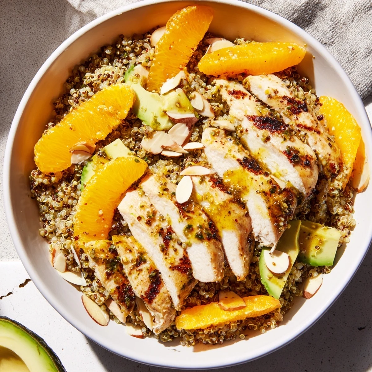 Bright citrus herb chicken salad bowl with grilled slices, avocado, orange segments, and toasted almonds over mixed greens and quinoa, drizzled with zesty dressing.