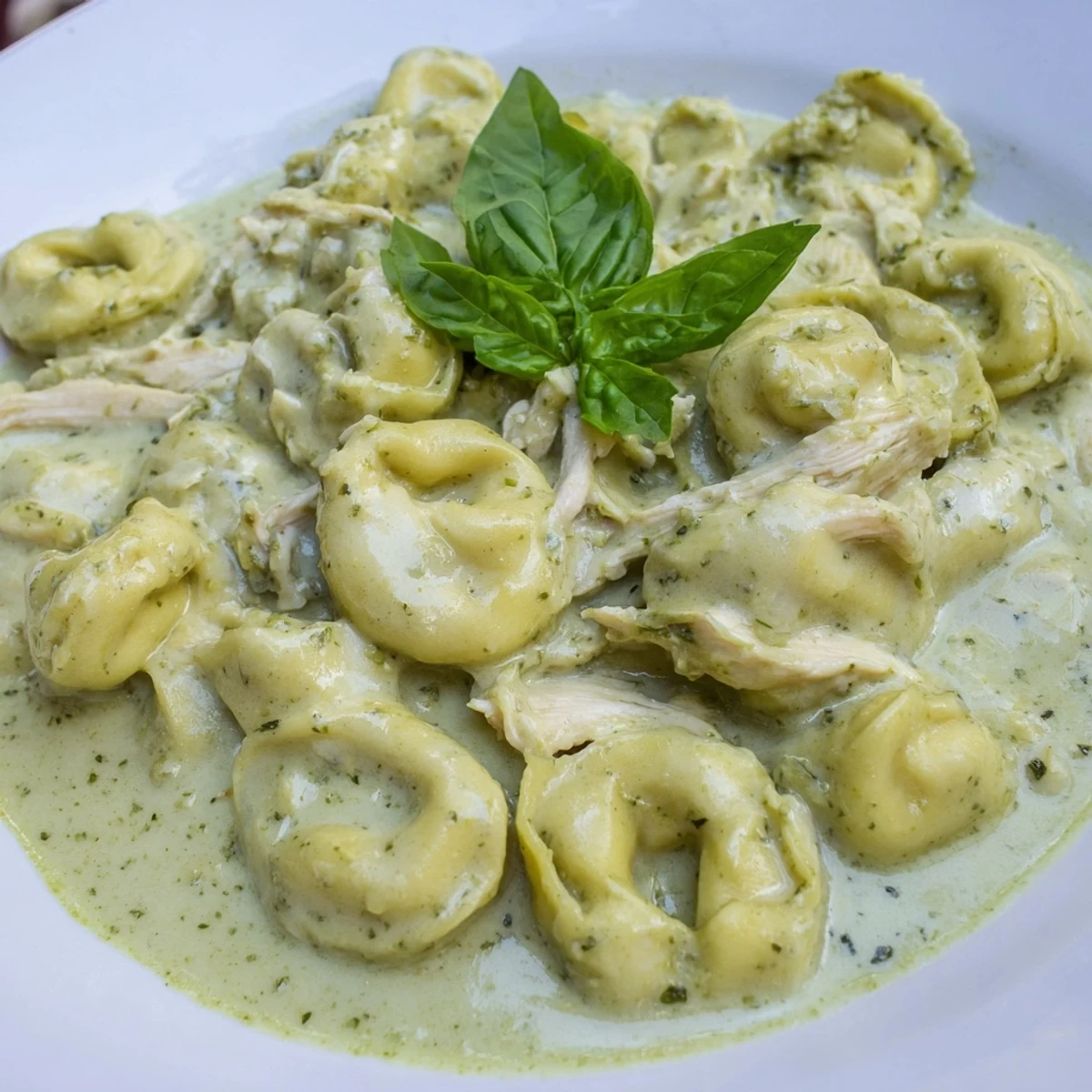 A close-up of Creamy Pesto Tortellini Skillet in a skillet, with melted Parmesan and vibrant green basil garnish.  