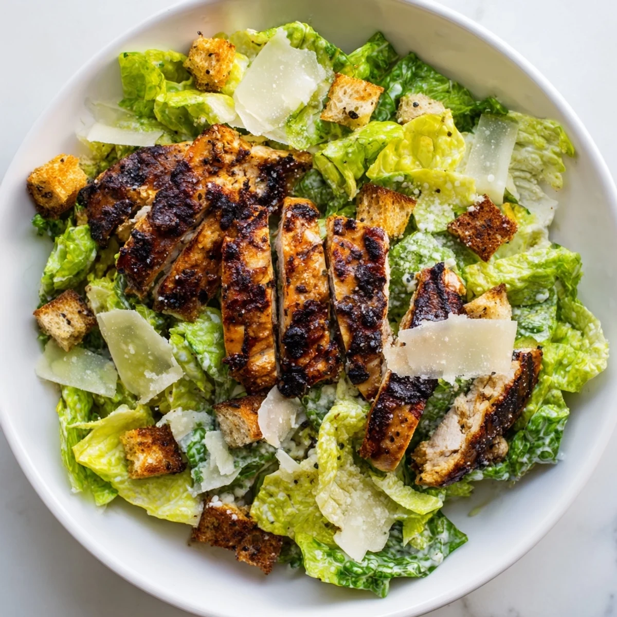 Grilled chicken strips rest on crisp romaine lettuce in this Yogurt Caesar Grilled Chicken Salad, topped with creamy dressing.