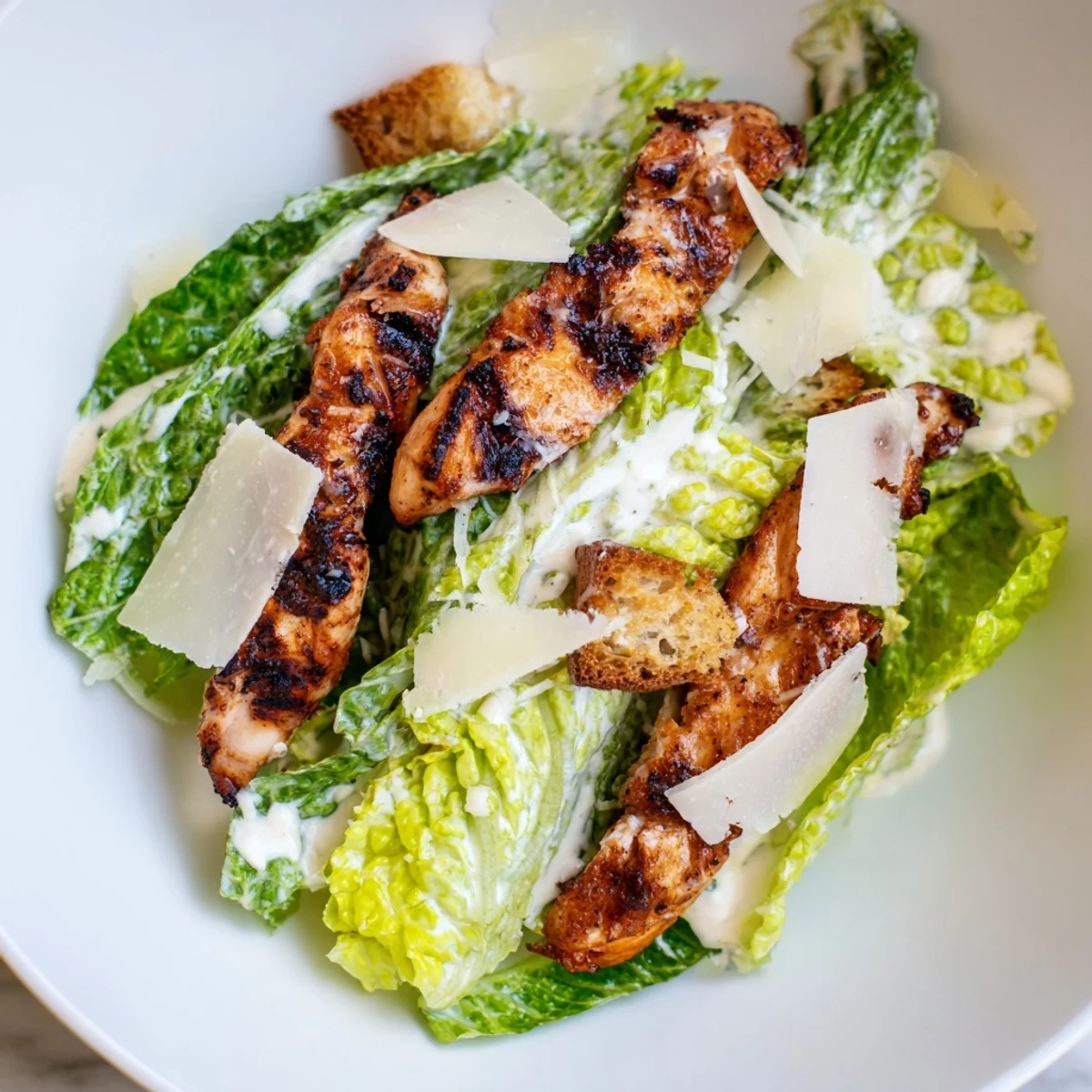 Sliced grilled chicken and shaved Parmesan garnish a vibrant Yogurt Caesar Grilled Chicken Salad on a rustic table.