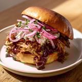 A close-up of delicious fire-kissed BBQ pulled pork, revealing tender, shredded meat on a bun.