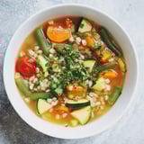 Close-up of a rustic Simple Homemade Grain and Vegetable Soup brimming with colorful vegetables and barley.