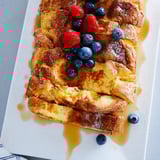A close-up of Soft Spice Baked French Toast Casserole, garnished with fresh berries and drizzled maple syrup.