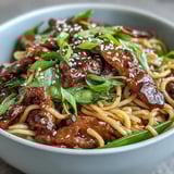 Close-up of Pork Noodle Stir-Fry showing steam rising from noodles, colorful veggies, and sesame seeds on top.