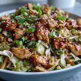 Fork lifting tender chicken, shredded cabbage, and carrots from a colorful Asian-inspired dinner bowl.