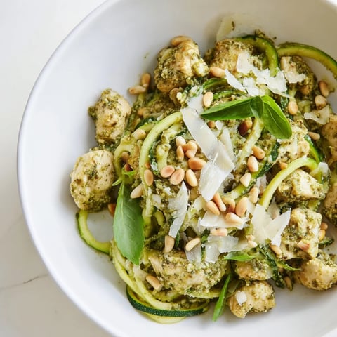A vibrant bowl of Pesto Zucchini Chicken Bowl featuring golden sautéed chicken, spiralized zucchini noodles, and a generous drizzle of basil pesto garnished with pine nuts.