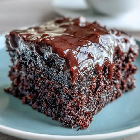 Easy Chocolate Fudge Cake sliced on a plate, revealing a moist crumb and rich, glossy chocolate icing.