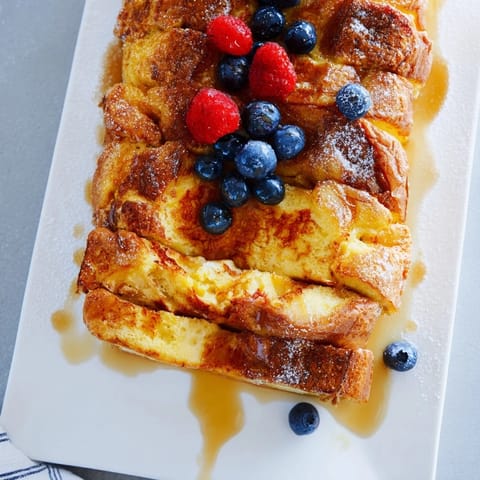 A close-up of Soft Spice Baked French Toast Casserole, garnished with fresh berries and drizzled maple syrup.