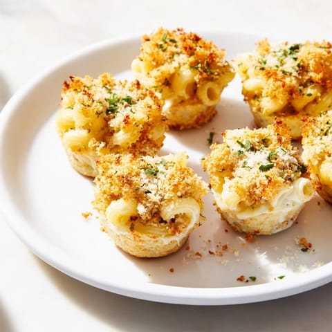 A close-up of cheesy Tinis Mac and Cheese cups, showing crispy breadcrumb topping and melted cheese beneath.