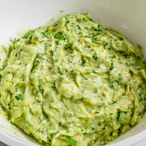 Bright green avocado lime dip garnished with cilantro, ready to serve with veggies.