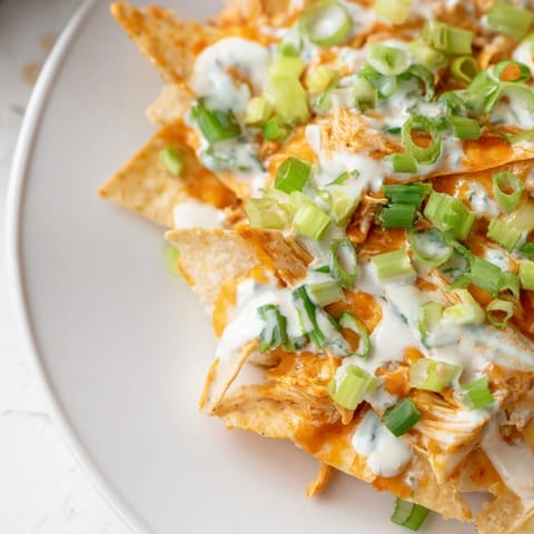 Fresh green onions and celery top a batch of hot Buffalo chicken nachos, ready for game day.