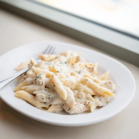 Glossy, creamy sauce coats the pasta and chicken in this baked Chicken Alfredo Casserole, garnished with fresh green parsley.