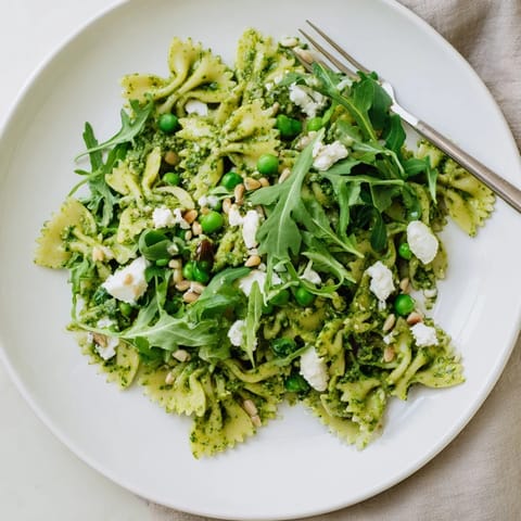 Spring Green Pesto Pasta Salad served cold with peas and arugula on a rustic table.
