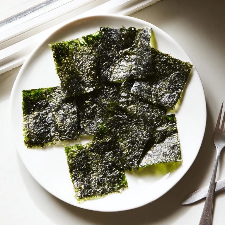 A hand holding a stack of golden Roasted Seaweed Chips, ready to be enjoyed as a healthy vegan snack.
