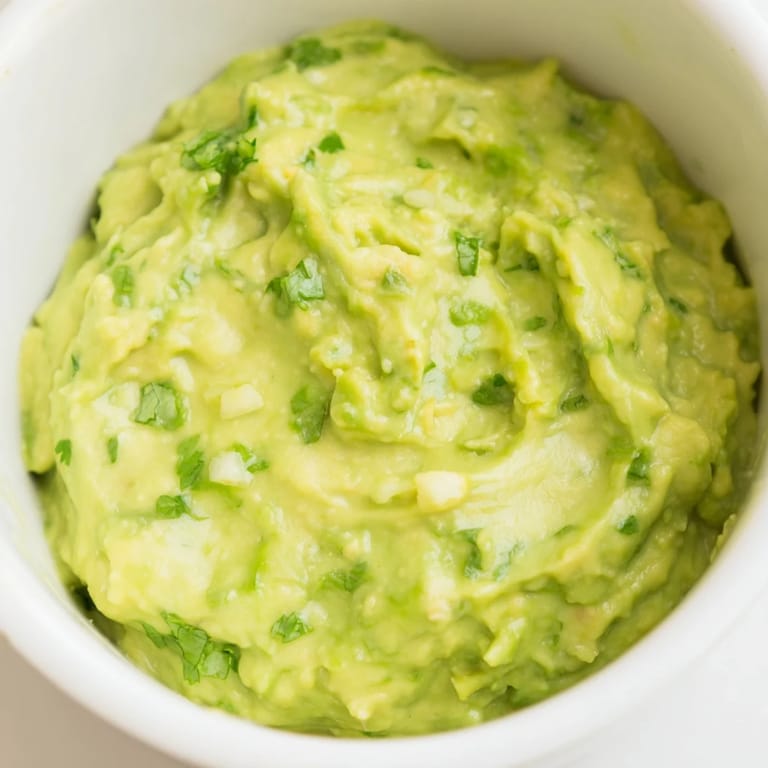 Zesty avocado lime dip spread on a toasted tortilla chip with a squeeze of lime.