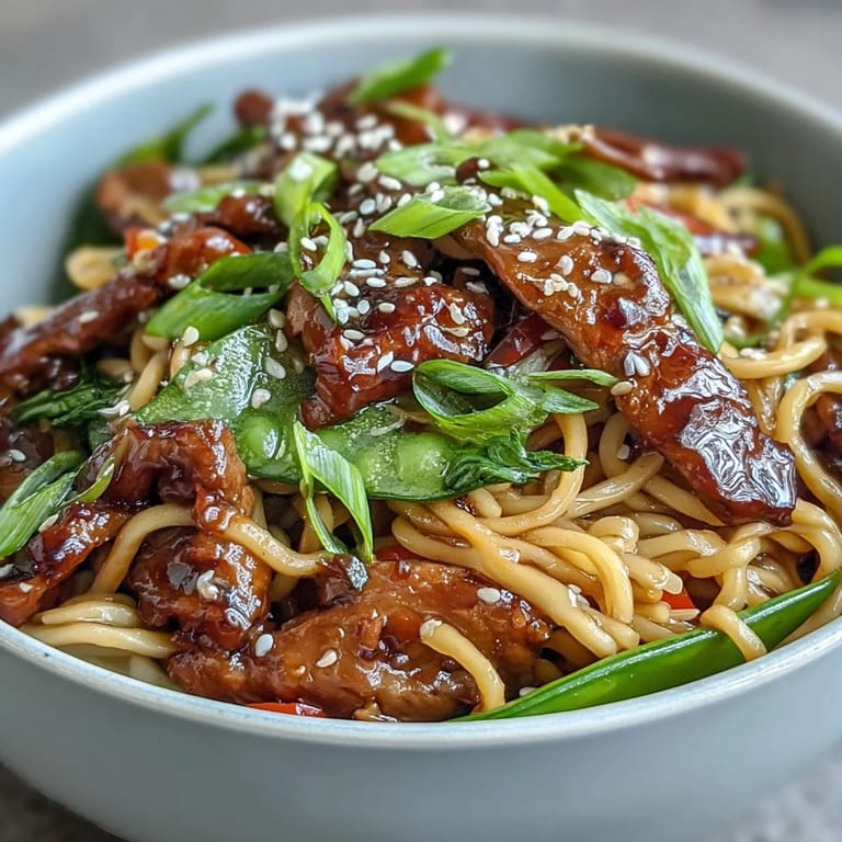 Close-up of Pork Noodle Stir-Fry showing steam rising from noodles, colorful veggies, and sesame seeds on top.