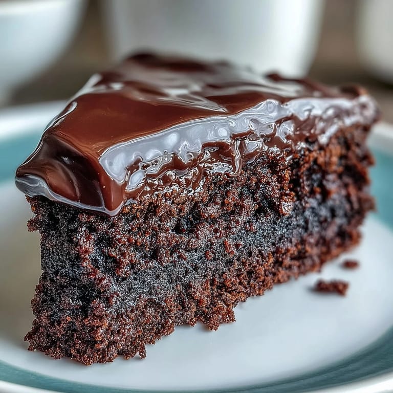 A close-up of Easy Chocolate Fudge Cake layers with silky-smooth chocolate frosting and a cup of milk.